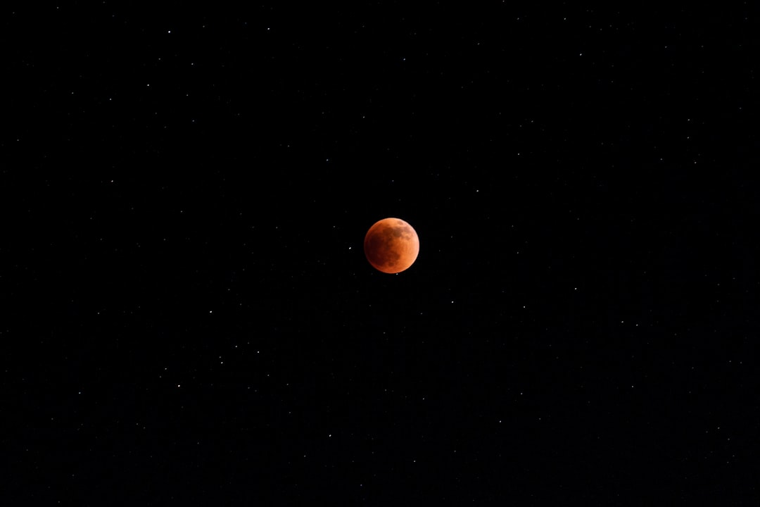 a red moon is seen in the dark sky