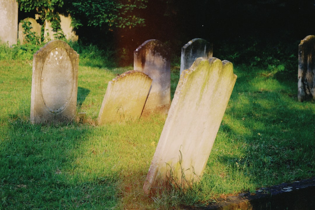 Weathered gravestones stand amidst green grass.