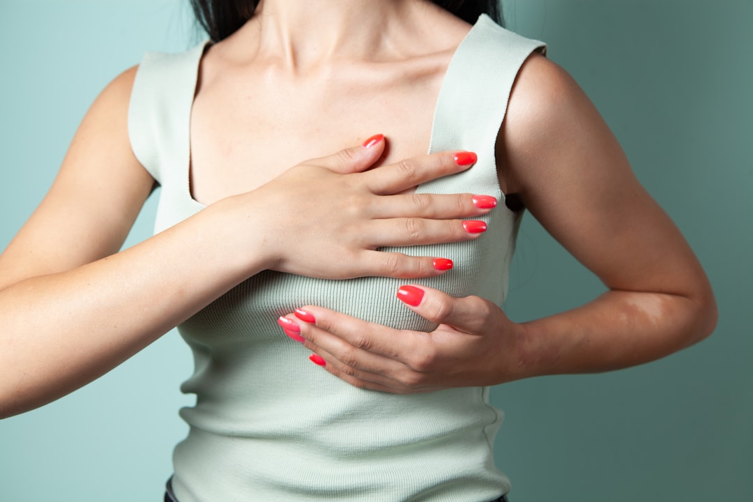 Woman performing breast self-examination against a teal background.