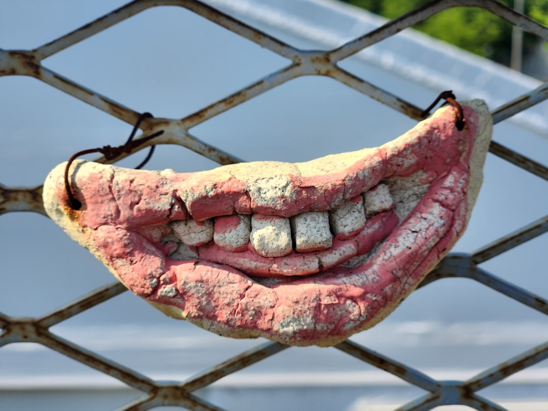 A cracked mouth mask hung on a metal fence.